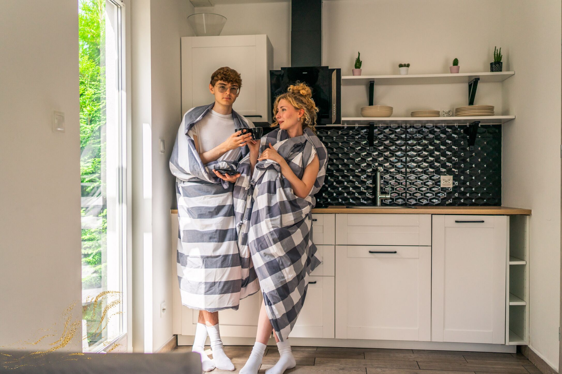 Une cuisine moderne avec des meubles blancs, un pare-feu noir et une fenêtre donnant sur un paysage verdoyant.