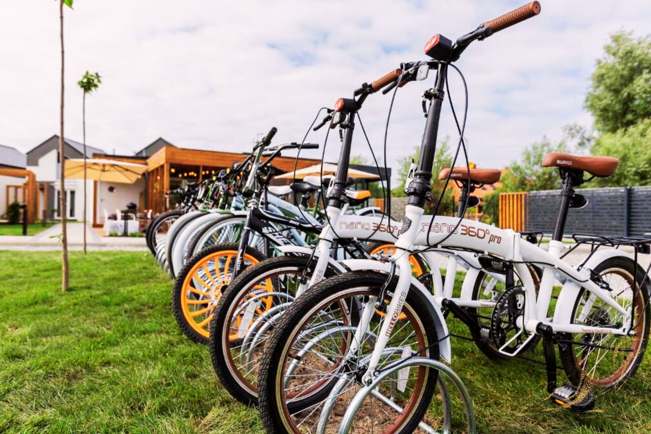 Une rangée de vélos blancs aux roues orange est garée sur une pelouse, avec un bâtiment en arrière-plan.