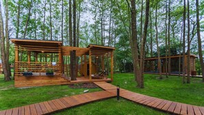 A wooden cabin with a deck and seating area, surrounded by trees. - Baltic Natur Park - Apartament B (Niechorze)