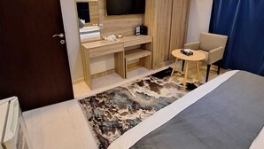 A hotel room with a bed, a desk with a flat-screen TV, a chair, and a small table. - agnehat alsmo hotel (Al Aydabi)
