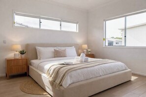 A bedroom with a large bed, two bedside tables with lamps, a window, and a view of the outside. - 5BR Executive Retreat in Rochedale | Perfect for families (Rochedale)