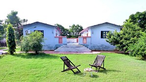 A two-story building with a red and white facade, a central staircase leading to the entrance, and two outdoor lounge chairs with a small table.