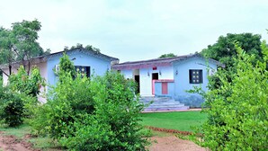 A two-story building with a blue facade and a red door, surrounded by greenery.