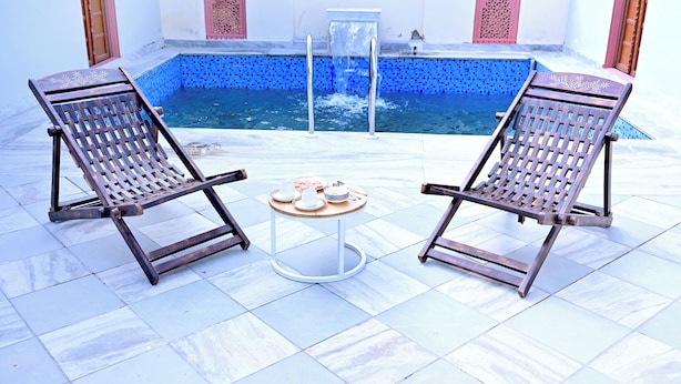 Two lounge chairs facing a pool with a small table between them.