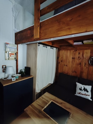 Ein gemütliches Blockhaus-Zimmer mit Holzbalkendecke, einem kleinen Schreibtisch mit Lampe, einer Uhr und einem Blumentopf.