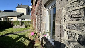 A stone building with a window and a door, surrounded by a grassy area and a hedge. - Sunny Sanctuary by the Town Center (Mont-Dore)