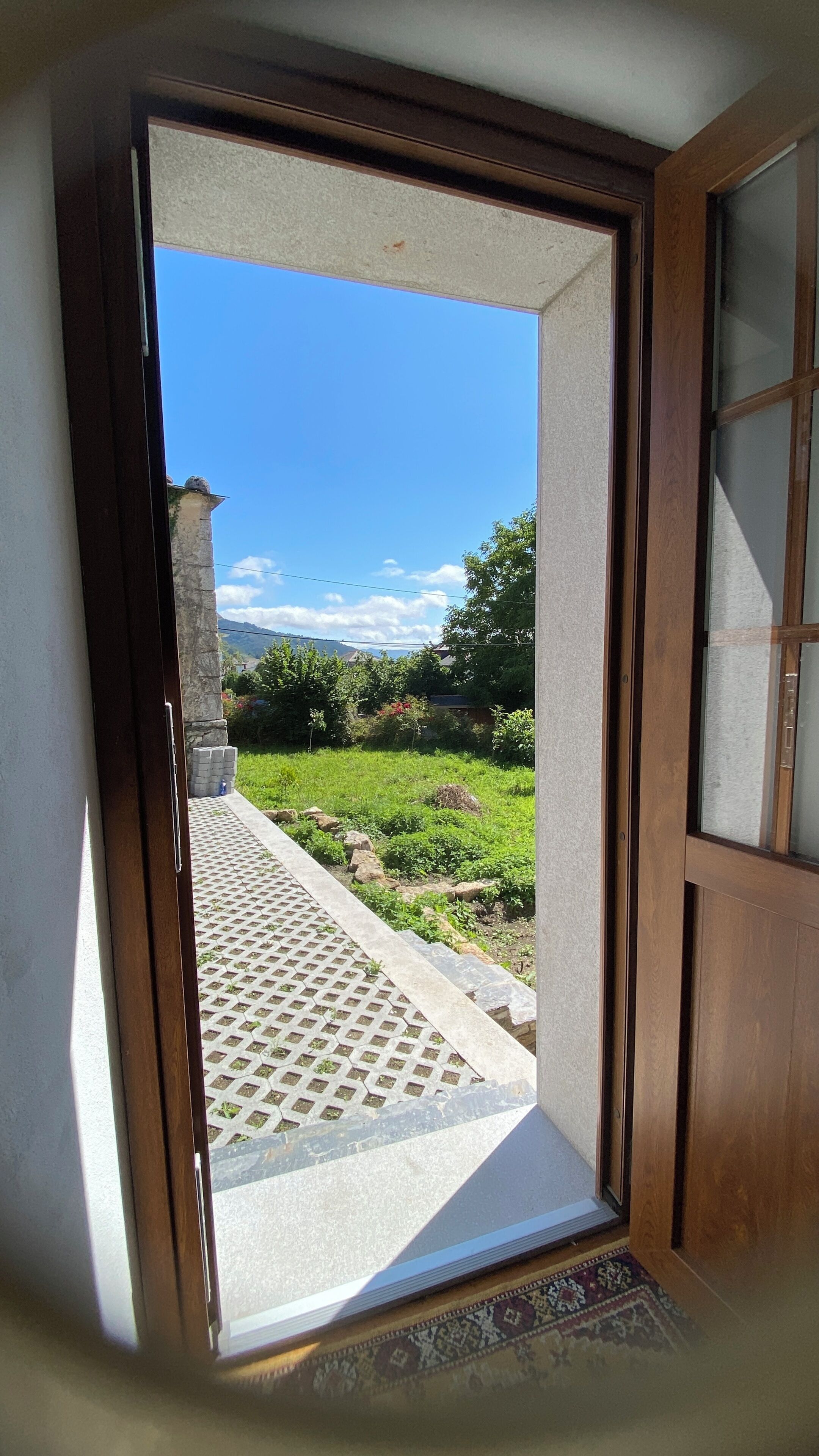 A doorway leading to a balcony with a view of a grassy area and a stone structure.