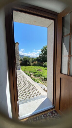 A doorway leading to a balcony with a view of a grassy area and a stone structure.