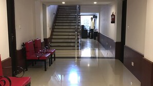 Un hall d’hôtel avec un escalier, des chaises rouges et un extincteur.