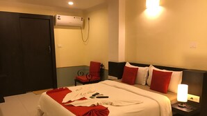 Une chambre d’hôtel avec un grand lit, une table de chevet avec une lampe, une chaise, un appareil de climatisation et une porte.