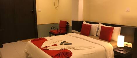 Una habitación de hotel con una cama grande, una mesita de noche con lámpara, una silla, un equipo de aire acondicionado y una puerta.