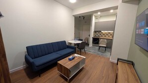 Un soggiorno moderno con un divano blu, un tavolino in legno e un'area da pranzo con sedie e un piccolo tavolo.