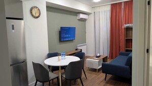 Un ambiente compatto con angolo ristoro, divano, televisione e frigorifero.