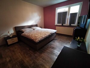 Une chambre à coucher comprenant un lit, une table de chevet, une commode, une fenêtre avec des stores et un téléviseur.