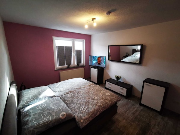 Une chambre à coucher avec un lit, une télévision, une commode et un miroir.