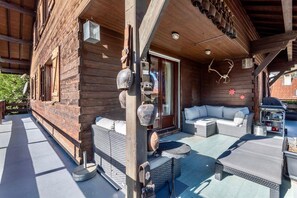 Una cabaña de madera con porche cubierto, mobiliario exterior y zona de barbacoa.