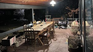 Terrassa exterior amb taula i caires de fusta, llum penjant i plantes en testos.