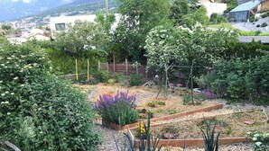 Un jardí amb alçades, diverses plantes i una vista d'una població al fons.