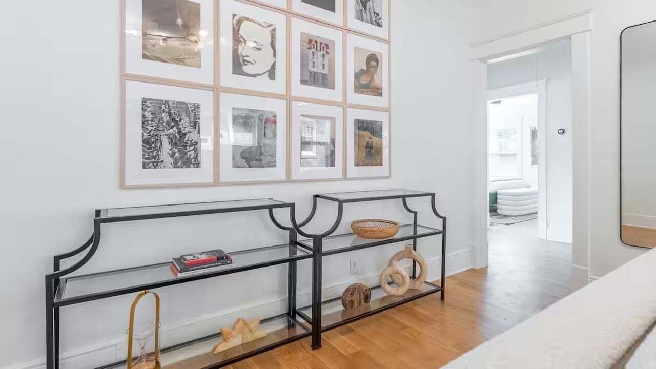 Ein modernes Wohnzimmer mit einem Glastisch, einem schwarzen Metallkonsole und dekorativen Gegenständen, sowie einer Wand mit gerahmten Bildern.
