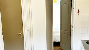 A hallway leading to a bedroom with a bed, a door, and a kitchen area. - Le Salers -Le Mont Dore 2pers (Mont-Dore)