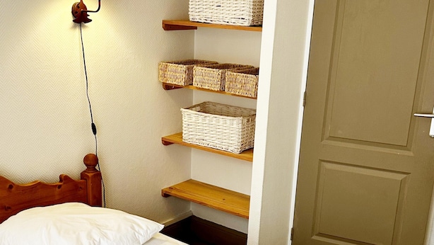 A bedroom with a wooden headboard, a bed with white bedding, and shelves with baskets. - Le Salers -Le Mont Dore 2pers (Mont-Dore)