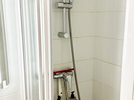 Una ducha con cabezal de ducha de mano y dispensador de jabón.
