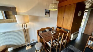A dining area with a wooden table and chairs, a floor lamp, a radiator, and a door leading to another room. - Tranquil Flat for 5 in Murat-le-quaire (Murat-le-Quaire)