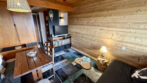 A cozy cabin interior with a wooden dining table, a TV, and a bookshelf. - Tranquil Flat for 5 in Murat-le-quaire (Murat-le-Quaire)