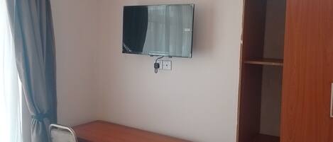 Une pièce comprenant un bureau en bois, une chaise, un téléviseur fixé au mur et une armoire.