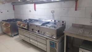 Ett professionellt kök med rostfria köksmaskiner, inklusive en spis, ugn och köksfläkt.
