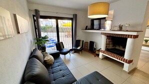 Sala de estar com sofá, cadeiras, lareira e vista através de uma porta de vidro.