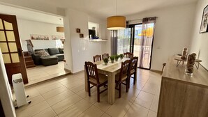 Uma sala de jantar moderna com uma mesa e cadeiras de madeira, uma janela grande com cortinas, e vista para o exterior.