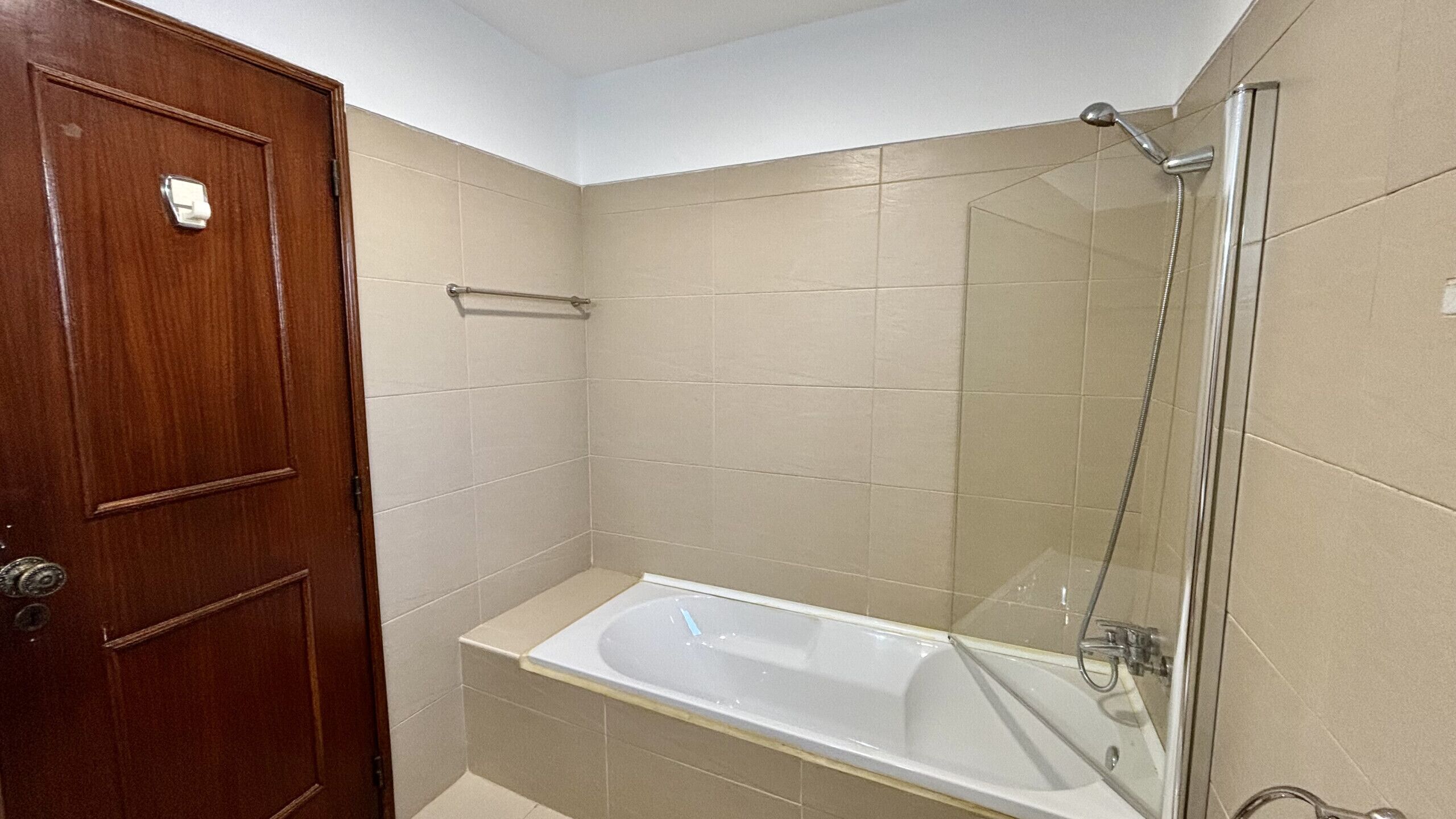 A bathroom with a wooden door, a glass shower enclosure, and a white bathtub.