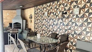 Een terras buiten met een ronde tafel, rieten stoelen, een bakstenen muur met geometrische patronen en een barbecuehoek.