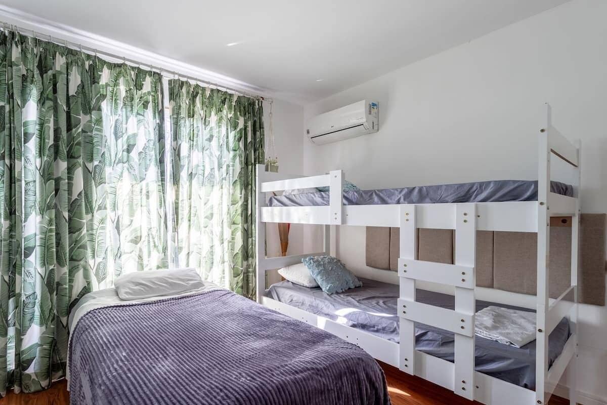Een kamer met een stapelbed, een enkel bed en een raam met gordijnen.