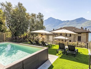 Ein Pool mit Liegestühlen, eine Rasenfläche, Sonnenschirme und Blick auf Berge.