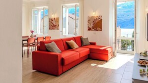 Una sala de estar moderna con un sofá seccional rojo, un comedor con sillas y un balcón con vistas a las montañas.
