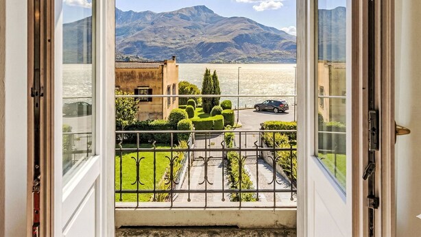 Vista desde una ventana que muestra un paisaje montañoso, un edificio con tejado de tejas y un coche estacionado en la calle.