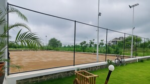 A tennis court with a wooden cart and a bicycle, surrounded by a fence and greenery. - Oasis Residency and Resorts  (Solapur)