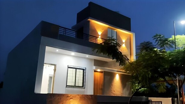 A modern two-story house with a balcony, large windows, and a well-lit entrance. - Oasis Residency and Resorts  (Solapur)