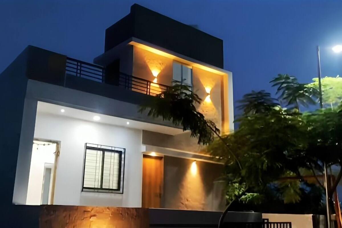 A modern two-story house with a balcony, large windows, and a well-lit entrance.