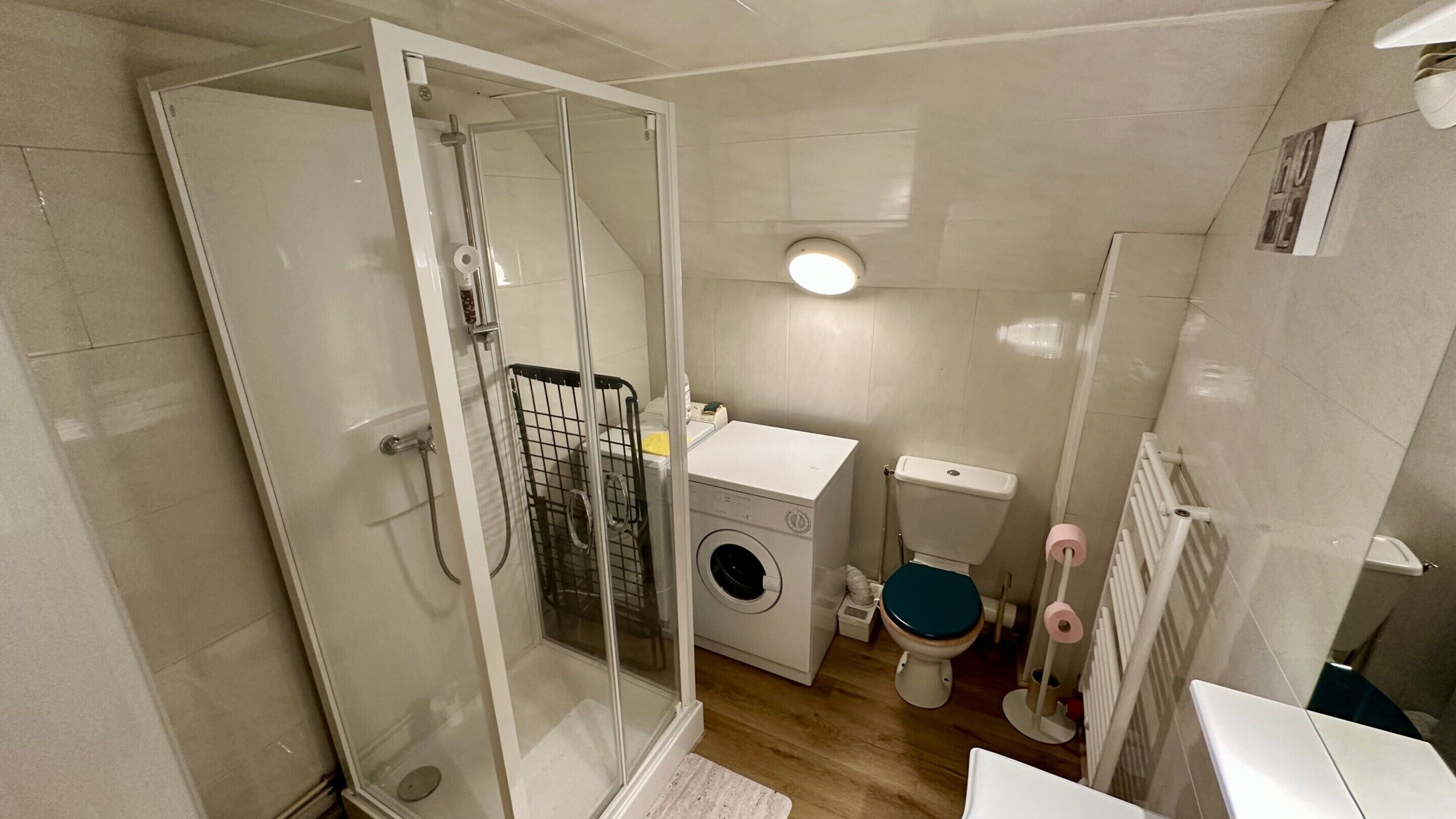 A compact bathroom with a glass shower enclosure, a washing machine, a toilet, and a radiator.