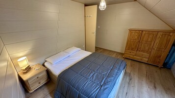 Un dormitorio con cama, mesita de noche, lámpara, armario y techo inclinado.