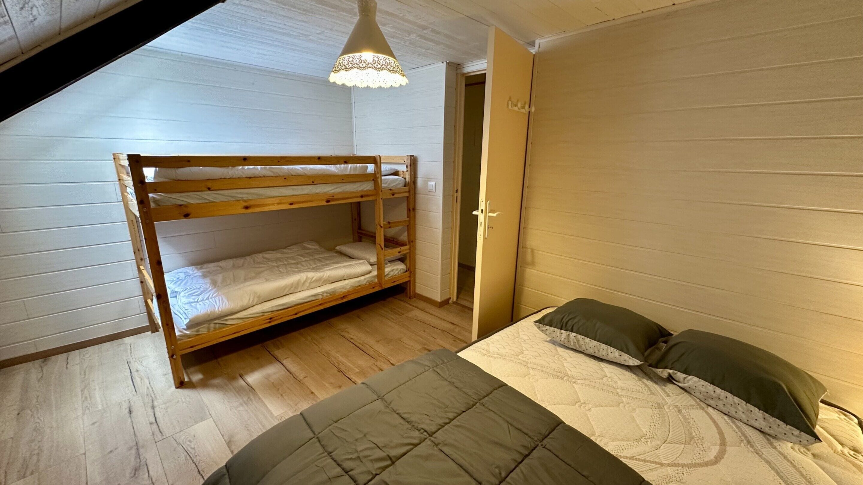 A dorm-style room with bunk beds, a door, and a bed with pillows.