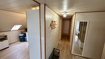 Un pasillo estrecho con suelo de madera, una pequeña zona de cocina con un lavabo y papeleras, y un perchero en la pared.