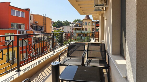 A balcony with a table and chairs, overlooking a row of colorful buildings. - Plovdiv City Centre One-Bedroom Apartment View Fully Equipped Kitchen City View (Plovdiv)