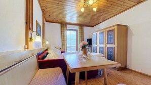 A room with a wooden ceiling, a dining table, benches, a cabinet with decorative panels, and a window with curtains.
