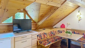 L’intérieur chaleureux d’un chalet avec un plafond en bois, une table à manger avec des bancs, un téléviseur et un petit réfrigérateur.