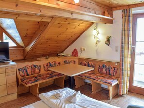 Une pièce chaleureuse avec un plafond en bois, un banc servant de coin salon, un lit et un téléviseur.