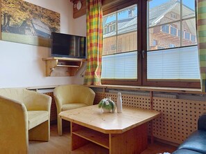 Een gezellige zithoek met een televisie, twee stoelen, een tafel en een raam met luxaflex.